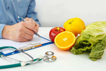 Nutritionist doctor writing diet plan on table. Right nutrition and slimming conceptの写真素材