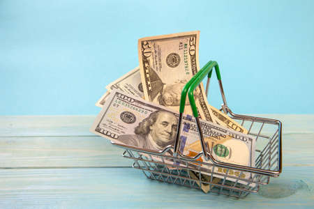 Shopping cart with paper dollar bills on light blue background