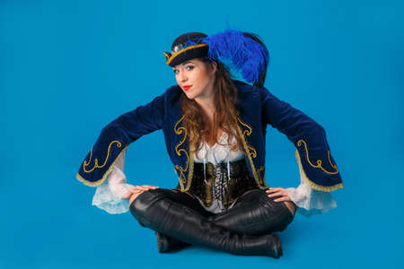 Studio portrait of a woman in a carnival pirate costume with a hat with a feather on a blue background.の写真素材