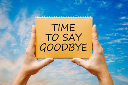 Man holding a card with text TIME TO SAY GOODBYE on the background of a blue sky.の写真素材