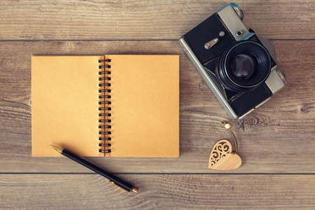 Notepad with pen and retro photo camera on wooden surface