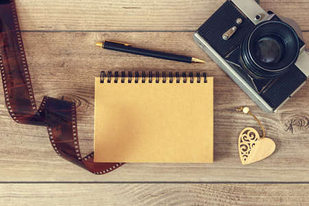 Notepad with pen and retro photo camera on wooden surfaceの写真素材