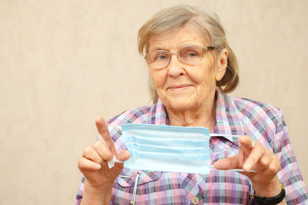 An elderly woman shows to wear a protective mask. Woman worries about coronavirusの写真素材