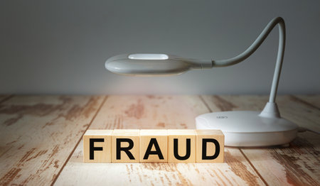 A table lamp illuminates wooden blocks with the word FRAUD.の写真素材