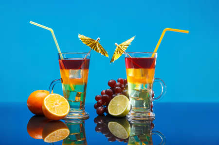 Two bright summer cocktails in a glass and fruit on a blue background