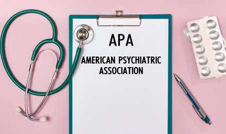 Paper with APA American Psychiatric Association on the office desk, stethoscope and pills, top viewの写真素材