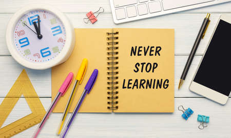 Never Stop Learning - an inscription on a notebook on a table with a clock and office supplies. Business conceptの写真素材