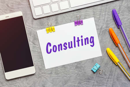 A paper note with the text of the Consulting, keyboard and a smartphone.