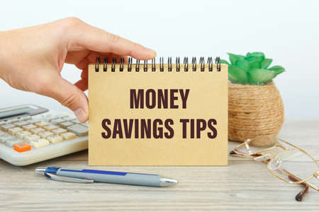 Notebook with the text MONEY SAVINGS TIPS on the office table among the stationery.の写真素材