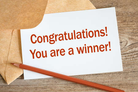 Open craft envelope and card with the words Congratulations - you are a winner, pencil on a wooden surface.の写真素材