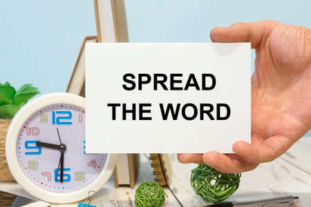 Spread the word - text on a card in your hand next to office suppliesの写真素材