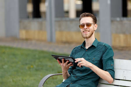 A young man in sunglasses holds a tablet in his hands, reads information on the tabletの写真素材