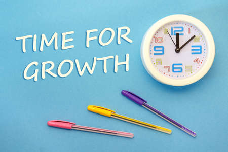 TIME FOR GROWTH - lettering on a blue background, clock and pensの写真素材