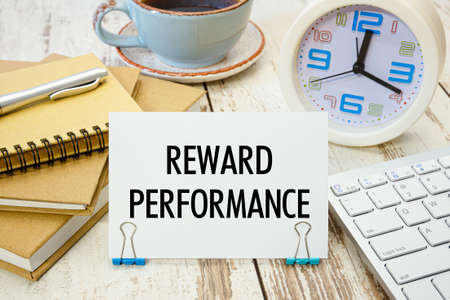 A sign with the inscription REWARD PERFORMANCE on the table with a calculator, coffee and notebooksの写真素材