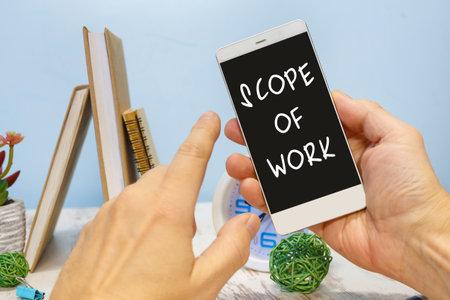 Smartphone in hand with the inscription Scope of Work next to office suppliesの写真素材