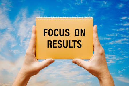 Man holding a card with text Focus on results on the background of a blue sky.の写真素材