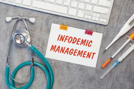Paper with INFODEMIC MANAGEMENT on the office desk, stethoscope and keyboard, top viewの写真素材