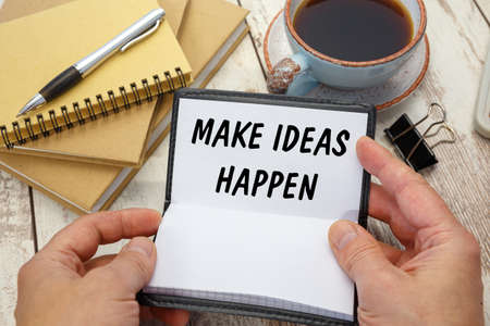Hands open a notebook with the inscription MAKE IDEAS HAPPEN on the background of the office deskの写真素材