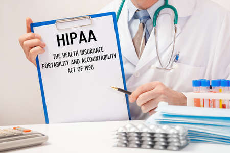 Doctor holds paper with inscription HIPAA The Health Insurance Portability and Accountability Act of 1996, stethoscope and pills on tableの写真素材