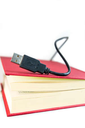 USB calbe coming out of a book with red covers. Ebook concept, audio book concept or information technology. Isolated on white.の写真素材
