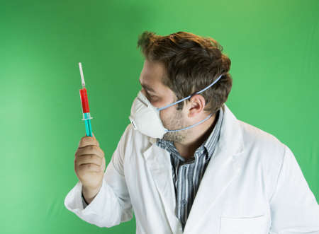 Young doctor with mask analising a syringe with blood sample.の写真素材