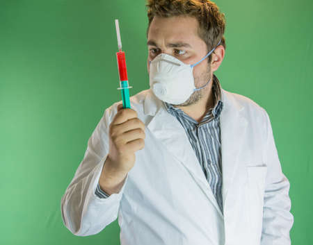 Young doctor with mask analising a syringe with blood sample.の写真素材