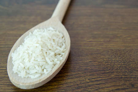 Long grain rice. Pile of rice in a wood spoon on a wooden table.の写真素材