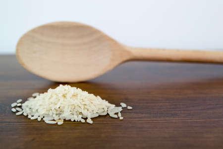 Pile of long grain rice on wooden table with blurry wood spoon in background.の写真素材
