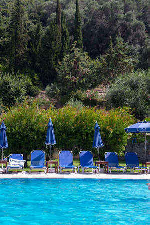Pool with blue sunbeds and umbrellas in a green forest.の写真素材