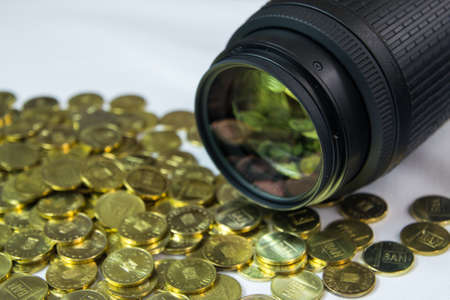 Photo lens with money reflection on the glass and pile of coins in the foreground.の写真素材