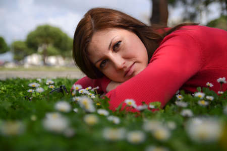 A portret of a young woman lying on green grass with white flowers.の写真素材