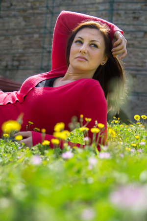 Portrait of a young woman lying on green grass with yellow flowers.の写真素材