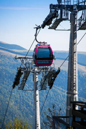 Glass cable car between two pylons going downhill. Forest and mountain landscape in the background on a sunny day.の写真素材