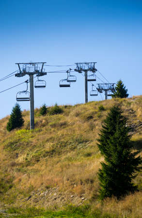 Empty chairlift in autumn landscape with green pine trees and hay. Blue sky in background.の写真素材