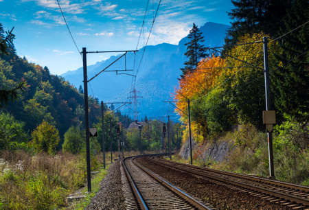 Double electrified railroad in autumn landscape. Trees with yellow leaves and blue sky. Mountains in far background.の写真素材