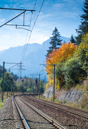 Double electrified railroad in autumn landscape. Trees with yellow leaves and blue sky. Mountains in far background.の写真素材