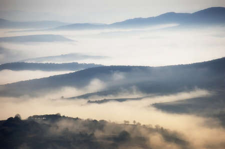 Fog above the mountains on a cold autumn morning with trees far awayの写真素材