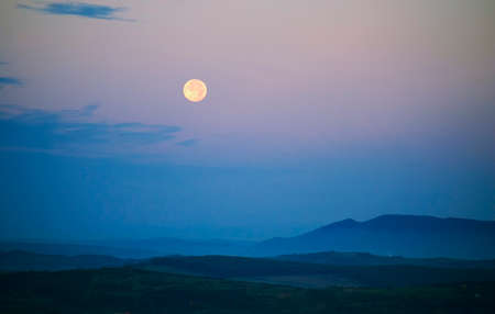 Moon rising over landscape with blue lightの写真素材