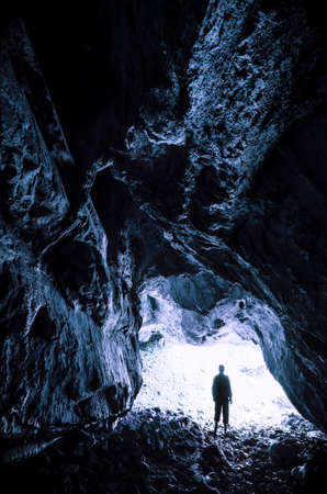 Man silhouette at dark cave entrance. Cave exploration in dark mysterious cave
