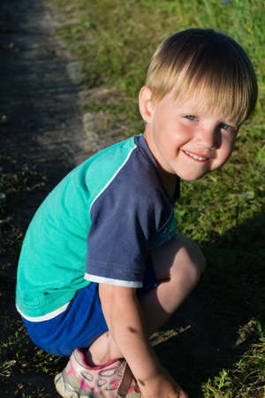 little boy in shorts sitting on grass and smilingの写真素材