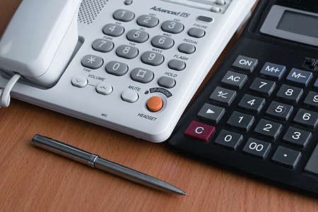telephone, calculator and metal ballpoint pen lying on a light wooden table in the office at work, preparing for the working day and making cold calls to clientsの写真素材