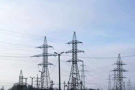 Several metal electricity pylon in the field. Cloud blue sky, slight haze. The supports holding the wire. Visible tops of the trees.の写真素材