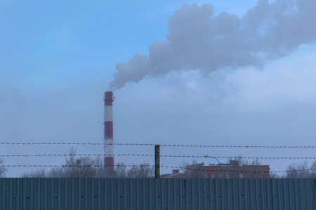 high pipe CHP on the background of blue sky, fog, smog, and out clouds of thick smoke, pipe red-and-white, it's cold outsideの写真素材