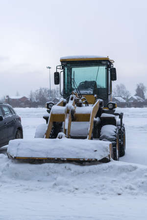 yellow wheeled snow plow tractor with a bucket all covered with snow stands on the cleared the Parking lot after a heavy snowfallの写真素材