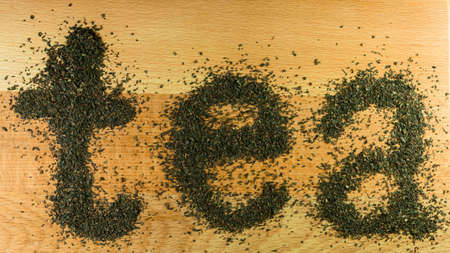 The word tea is laid out on a light-brown wooden Board small leaf black tea. Board is the background for the word tea.の写真素材
