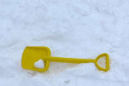 Children's yellow plastic shovel lies a frosty day on the white crisp snow. In the blade lies a snowball in the shape of a heart.の写真素材
