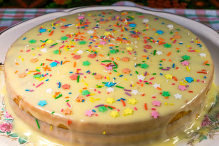 On a table covered with a tablecloth, a plate. On the plate of sponge cake. Cake drizzled in custard. Made with your own hands. For gift-giving for the holiday. Decorated with a sprinkling of stars and sticks different colors.の写真素材