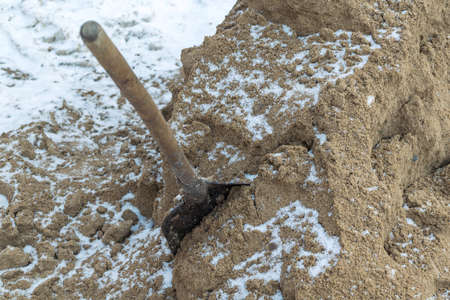 On the street is a big pile of frozen sand. Stuck in the sand a dirty shovel with a wooden handle. Snow, winter. Sand for sprinkling roads and sidewalks. That was not slippery and people fell.の写真素材