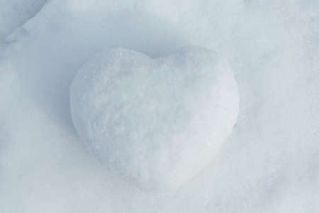 In winter the white snow lies cobbled together a snowball in the shape of a heart. On the street the day and the sun is shining. Cold and frosty. Can be used as a gift, a surprise.の写真素材