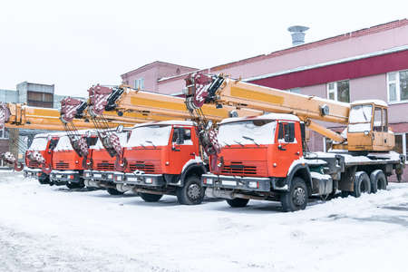 The Parking lot is a few truck cranes orange and yellow colors. Winter, all the cranes covered with snow. Mechanism of truck crane telescopic type. The hook on the ropes.の写真素材